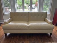 Front view showing two seat cushions, button-tufted back, track arms and wooden legs