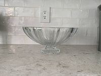 Front view of the large clear crystal bowl placed on a kitchen countertop with a white tiled backsplash.