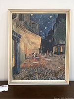 Front view of framed artwork showing the scene of a café terrace at night by Vincent Van Gogh with visible water damage bottom right.