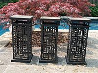 Front view of the set of three Asian inspired metal candle holders showing geometric cutout patterns and flat tops outdoors near a pool.