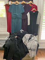 Photo showing hanging dresses and folded jackets including rust red sleeveless, teal gathered waist, purple wrap dress, black dress with silver sleeves, and folded black and patterned jackets.
