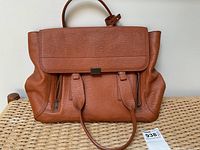 Front view of cognac pebbled leather satchel on woven bench