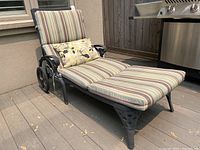 Chaise lounge with striped cushions and floral pillow on wooden deck next to grill