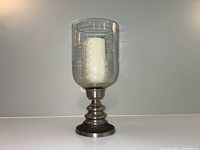 Front view of the vintage style glass hurricane candle holder with pewter base and included candle inside.
