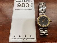 Front of watch showing dial, bezel and portion of bracelet alongside MaxSold lot card