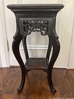Front view of carved wood pedestal table showing square top, curved legs and carved apron