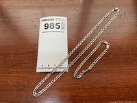 Full view of sterling silver chain necklace and matching bracelet placed on wood surface with MaxSold tag