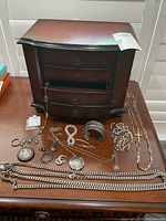 Full view of mahogany jewelry chest with four drawers and various jewelry items spread on top including necklaces, bracelets, earrings, and keychain.