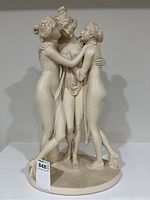 Front view of the Three Graces plaster sculpture showing three nude embracing female figures on an oval base.