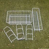 Five white wire organizer items arranged on grass including a large basket, narrow rack, and three smaller vertical racks.
