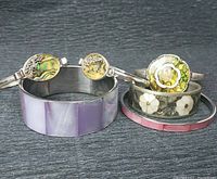 Top view of six mixed age boho style bracelets showing abalone, mother of pearl, lilac resin cuff, and pink enamel bangle