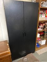 Tall black metal cabinet with closed doors showing black handles, scuff marks visible