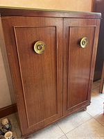 Front view of the wooden storage chest showing two paneled doors and brass circular handles.