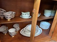 Wide view of the china set inside a wooden cabinet showing cups, plates, and saucers stacked and arranged