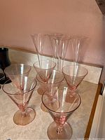 Six clear classic champagne flutes standing behind six pink-tinted martini glasses on a kitchen counter.