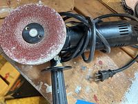 Close-up of the 4.5-inch disc grinder showing the disc with wear and attached side handle, power cord coiled.
