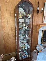 Full view of tall wooden curio cabinet filled with collectible figurines (not included). Shows curved top and glass shelves.