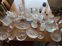 Wide view of all glass and crystal items on wooden table including bowls, decanter, dishes, shakers, and napkin holder.