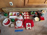 Overview of holiday and winter themed kitchen and decorative items laid on carpet in front of wood-paneled wall.