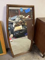 Full-length rectangular mirror leaning on wall beside furniture, showing full mirror and frame shape