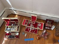 Open cream jewelry box showing red velvet trays with assorted jewelry and coin sets