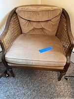 Angle showing front and left side of mid century wooden chair with cane sides and a brown cushioned seat and back with tufted button detail.