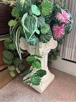 White classical-style plant pedestal stand holding a pot with multiple leafy plants.