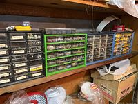 Wide shot showing multiple black and green organizer units with drawers containing various metal and plastic fasteners and hardware components.