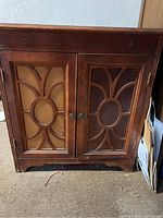 Front view of the small wooden chest with decorative glass panel doors, missing two knobs.