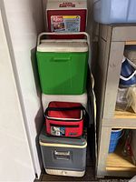 Stack of six coolers including Little Playmate Igloo, green/white hard cooler, red soft cooler, grey hard cooler and cream large cooler