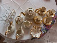 Full view of the tea set, candy dish, and shot glasses displayed on tablecloth with floral accents