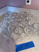 Clear glass stemware pieces with silver rims on a counter, arranged in rows, close-up view.
