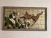 Full frontal view of framed wall art showing two birds in flight, flower cluster and stone wall background.