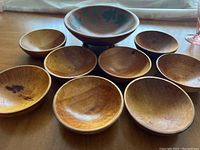 Set of nine wooden bowls on a table, showing one large bowl and eight smaller bowls with wood grain and wear marks.