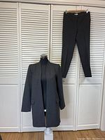 Full view of the Calvin Klein women's grey/black pants suit featuring the open jacket on a dress form and pants hanging beside it, showing the outfit's cut and style.