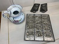 Photo showing the hand painted ceramic pitcher with floral and scalloped designs, two-piece bird chocolate mold, and the rectangular zoo animal chocolate mold