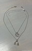 Two sterling silver necklaces with charms laid flat to show chain style and charm details. Double heart charm on one, wishbone charm on other.