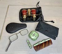 Overview photo showing all items: antique folding lorgnette glasses with damaged case, hand painted enamel cosmetics set with matching case, contemporary opera glasses with drawstring case.