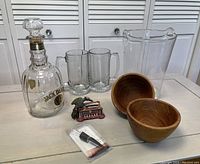 Photo showing all bar items on a white table: Crate & Barrel clear heavy glass ice bucket, vintage Jack Daniels No. 7 glass decanter (empty), antique metal bird toothpick dispenser, two wood bowls, red wine aerator and pourer, and two heavy glass mugs.