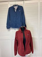 Photo showing two women's Columbia clothing items: a red microfleece jacket on a mannequin and a blue outdoor shirt hanging on a hanger.