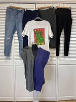 Photo showing six pairs of leggings hung on hangers and one white graphic T-shirt with a green Statue of Liberty design featuring a red background, all displayed against white closet doors.