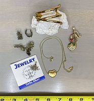 Photo showing entire jewelry lot with six items: Carlos Albert charm with certificate, puffed heart necklace, artisan acorn & leaf earrings and pin set, gold tone cuff bracelet, vintage Santa pin.