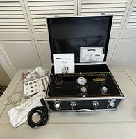 Photo showing New Spa Diamond Micro-Dermabrasion Machine in open black carrying case along with replacement filter tips, cords, air tubing, white cloth, and user manuals on a table.