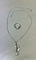 Full view of sterling silver necklace with multi-freshwater pearl drop pendant and freshwater pearl ring on gray surface.