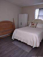 Photo of full bed frame headboard attached to a mattress with pillow and footboard standing nearby.