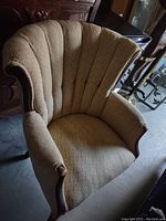 Photo of a scalloped Chanel style back chair with beige fabric upholstery and exposed carved wood arms. The upholstery shows wear and needs replacement.