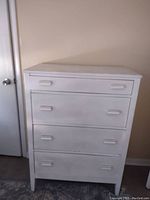 Front view of tall, ivory chest of drawers with four drawers and sleek rectangular pulls, showing shimmery finish and straight legs.