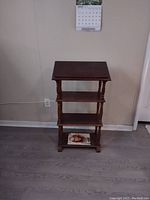 Photo of a wooden podium lectern stand with multiple shelves in a room against a wall under a calendar.