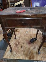 Full view of Singer sewing machine wooden cabinet with foot pedal on wooden floor, showing wear and dust on cabinet surface.