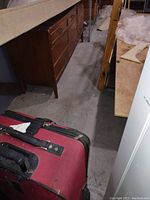 Photo showing red and black fabric suitcase on warehouse floor, with visible handle and zipper.